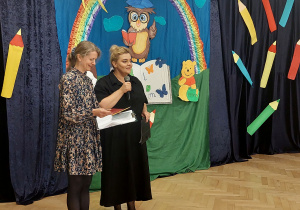 Pani Karolina i pani Justyna stoją z mikrofonem i witają gości.