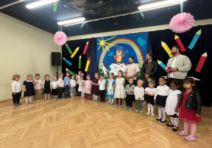 Nowe dzieci stoją na sali gimnastycznej w półkolu , z tyłu stoi kilku rodziców.