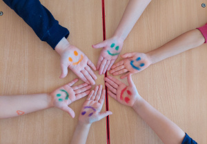 Sześcioro dzieci pokazuje prawą dłoń z namalowaną buzią .