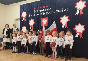 Dzieci przebrane na galowo stoją z flagą w ręku.