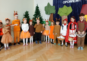 Grupa dzieci biorących udział w przedstawieniu. Widoczne dzieci przebrane za gajowego, 2 Czerwonych Kapturków i grupę wiewiórek.