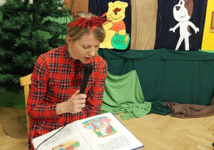 Nauczycielka czyta bajkę dzieciom, uczestnikom balu. W tle widoczna dekoracja: Kubus puchatek i Reksio oraz zielone drzewa.