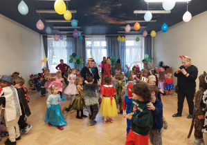 W sali dzieci tańczą w rytm muzyki przebrane w stroje karnawałowe.