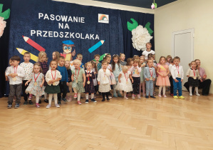 Na scenie stoją nowe przedszkolaki z medalami na szyi.