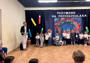 Po lewej stronie stoi nauczycielka prowadząca uroczystość. Dzieci stoja w jednej linii.