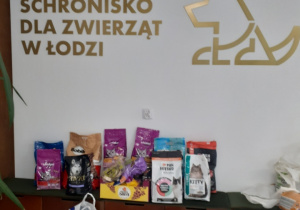 Na tle tablicy z napisem Schronisko dla zwierząt w Łodzi poustawiane są zebrane karmy dla zwierząt