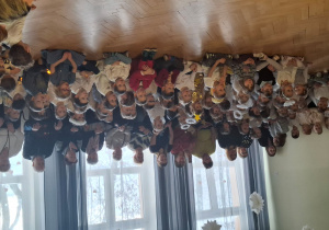 Na tle okien siedzą goście zaproszeni na uroczystość. Przed nimi siedzą dzieci z róznych grup przedszkolnych.