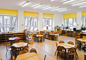 Klasa przedszkolna- z tyłu okna, dookoła szafki z pomocami na środku stoły z krzesłami