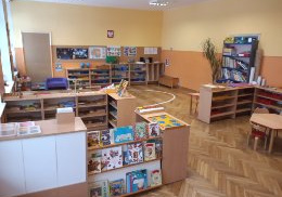 Klasa przedszkolna-dookoła znajdują się niskie szafki z pomocami rozwojowymi znajdujacymi się na półkach. Z przodu szafka z książkami dla dzieci.
