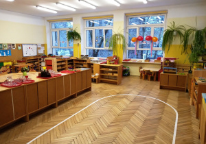Klasa przedszkolna- na podłodze namalowana biała linia w kształcie elipsy. Po lewej stronie rząd szafek na których ustawione są tace z naczynami do przelewania wody.